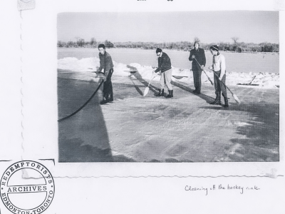 Black and white photo of four men cleaning an outdoor hockey rink.